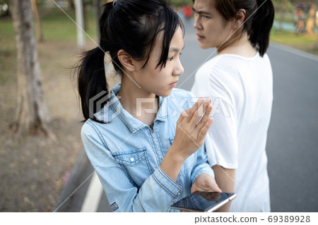Distracted child girl looking at phone,addicted to playing games on mobile phone,crashed into adult woman while walking on street,carelessness of asian teenage with female people bump into each other 69389928