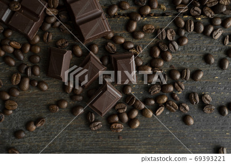 Roasted arabica coffee beans scattered on a wooden table with a bar of dark chocolate. Fresh coffee beans. Roasted arabica coffee beans scattered on a wooden table with a bar of dark chocolate. Fresh coffee beans. 69393221