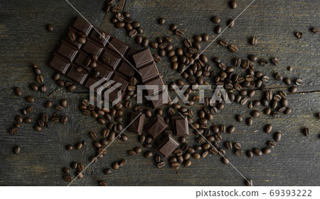 Roasted arabica coffee beans scattered on a wooden table with a bar of dark chocolate. Fresh coffee beans. Roasted arabica coffee beans scattered on a wooden table with a bar of dark chocolate. Fresh coffee beans. 69393222