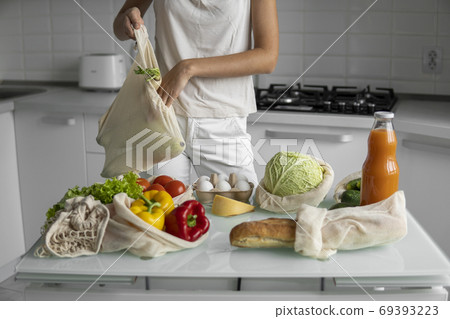 Woman hand holding Reusable eco textile grocery bag with vegetables and fruits. Zero waste and plastic free concept. Girl is holding mesh cotton shopper with vegetables. Woman hand holding Reusable eco textile grocery bag with vegetables and fruits. Zero waste and plastic free concept. Girl is holding mesh cotton shopper with vegetables. 69393223