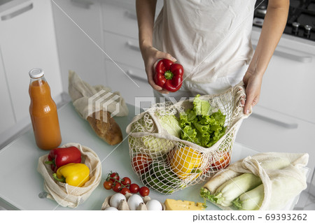 Woman hand holding Reusable eco textile grocery bag with vegetables and takes red and yellow pepper out. Zero waste and plastic free concept. Girl is holding mesh cotton shopper with vegetables. Woman hand holding Reusable eco textile grocery bag with vegetables and takes red and yellow pepper out. Zero waste and plastic free concept. Girl is holding mesh cotton shopper with vegetables. 69393262