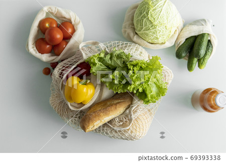 Eco friendly canvas grocery bag. Vegetables, fruits in reusable eco cotton bags and orange juice in a glass bottle on table. Zero waste shopping concept. Multi-use, reuse, recycle. 69393338