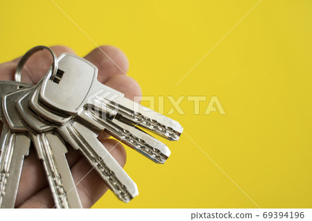 Mens hand holding a set of keys with a yellow background. Realtor with a keys to an apartment for a clients. Focus on the keys. Bunch of keys in a realtors hand. Mens hand holding a set of keys with a yellow background. Realtor with a keys to an apartment for a clients. Focus on the keys. Bunch of keys in a realtors hand. 69394196