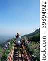 Young tourist woman on the wooden terrace with flowers, looking at mountain landscape with blue sky. 69394922