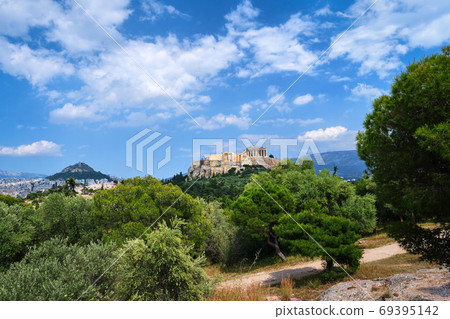 Iconic view of Acropolis hill and Lycabettus hill in background in Athens, Greece from Pnyx hill in summer daylight with great clouds in blue sky. Iconic view of Acropolis hill and Lycabettus hill in background in Athens, Greece from Pnyx hill in summer daylight with great clouds in blue sky. 69395142