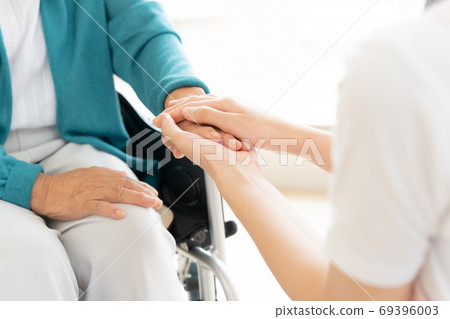 Caregiver holding the hand of a senior sitting in a wheelchair Caregiver holding the hand of a senior sitting in a wheelchair 69396003