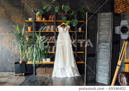 A chic silk wedding dress hangs on a bookcase. A chic silk wedding dress hangs on a bookcase. 69396802