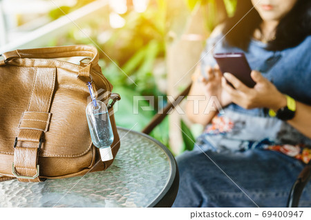 Mini portable alcohol gel bottle to kill Corona Virus(Covid-19) hang on a brown leather shoulder bag on table in garden. New normal lifestyle. Health care concept. Selective focus on alcohol gel 69400947