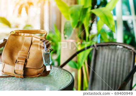 Mini portable alcohol gel bottle to kill Corona Virus(Covid-19) hang on a brown leather shoulder bag on table in garden. New normal lifestyle. Health care concept. Selective focus on alcohol gel Mini portable alcohol gel bottle to kill Corona Virus(Covid-19) hang on a brown leather shoulder bag on table in garden. New normal lifestyle. Health care concept. Selective focus on alcohol gel 69400949