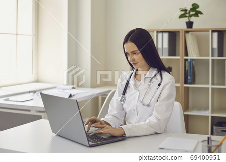 Young female doctor typing on laptop keyword surfing net in modern hospital office Young female doctor typing on laptop keyword surfing net in modern hospital office 69400951
