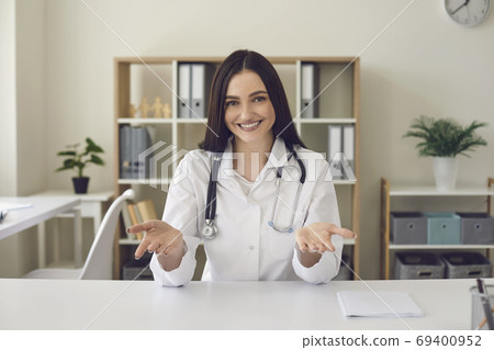 Smiling woman doctor looking at camera and showing something with hands in medical clinic Smiling woman doctor looking at camera and showing something with hands in medical clinic 69400952