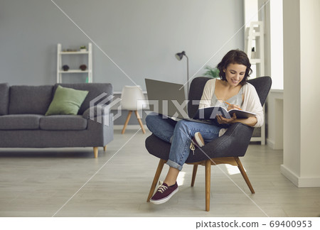 Smiling woman sitting at home with laptop and making notes during online lesson Smiling woman sitting at home with laptop and making notes during online lesson 69400953