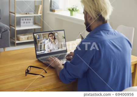 A young man is at home and calls a doctor online using a laptop. A female doctor on a laptop screen makes a medical consultation on the Internet. 69400956