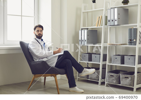 Man doctor therapist looking at camera, listening to patient and making notes in medical clinic 69400970