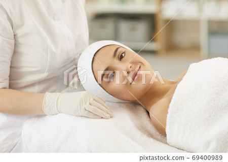 Smiling young woman looking at camera after procedure of facial massage Smiling young woman looking at camera after procedure of facial massage 69400989