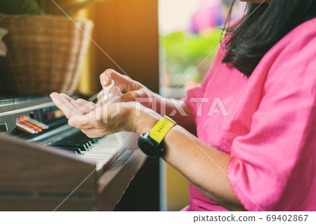 Hands of woman pressed a bottle of alcohol gel to wash her hands and kill the coronavirus (Covid-19) before playing with old organ in her home.New normal lifestyle.Health care concept.Selective focus 69402867