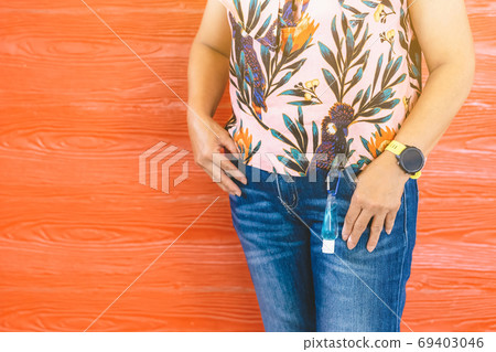 Mini portable alcohol gel bottle to kill Corona Virus(Covid-19) hanging on belt loop of woman' s jeans with plank background. New normal lifestyle. Health care concept. Selective focus on alcohol gel 69403046