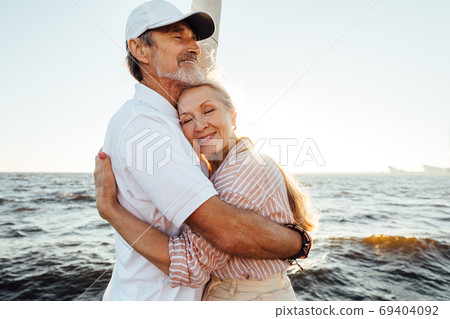 Affectionate senior couple embracing on private yacht. Beautiful mature woman leaning on husband's chest with eyes closed.	 69404092