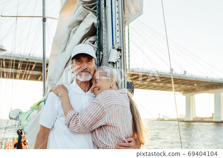 Portrait of affectionate mature couple embracing each other while standing on a sailboat. Senior couple enjoying their vacation. Portrait of affectionate mature couple embracing each other while standing on a sailboat. Senior couple enjoying their vacation. 69404104