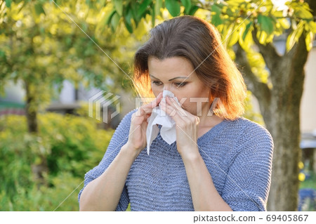 Seasonal allergies, woman with nasal wipe, sneezing, wiping nose outdoor 69405867