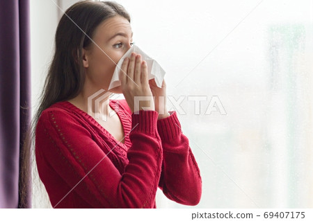 Female with cough, snot, temperature standing at home near window Female with cough, snot, temperature standing at home near window 69407175