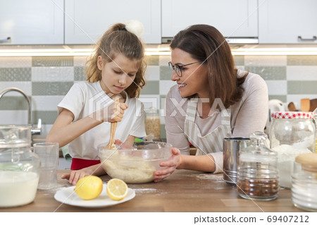 Mother and daughter child together at home kitchen preparing cookies Mother and daughter child together at home kitchen preparing cookies 69407212