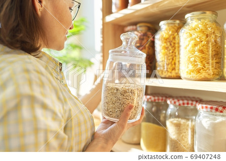 Food storage in pantry, woman holding jar of oatmeal in hand 69407248