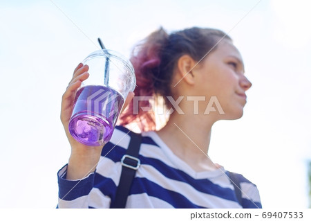Teen girl holding glass with straw with purple drink in hand Teen girl holding glass with straw with purple drink in hand 69407533