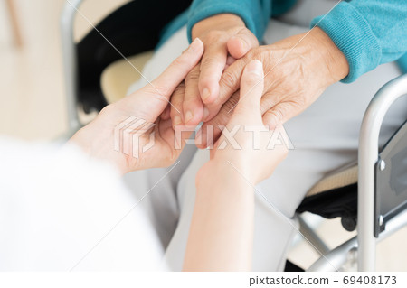 Caregiver holding the hand of a senior sitting in a wheelchair 69408173