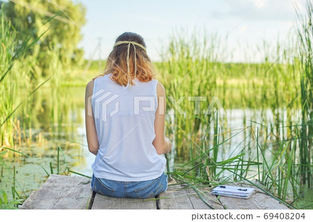 Young woman sitting with her back on wooden pier, copy space 69408204