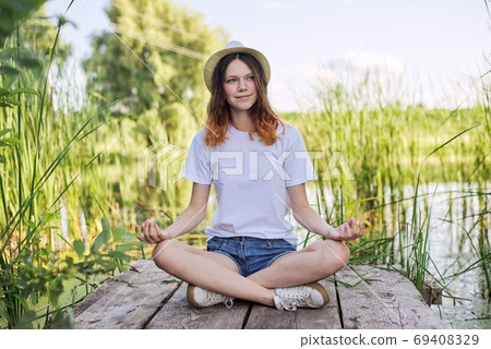 Teen girl sitting in lotus position, meditating on nature Teen girl sitting in lotus position, meditating on nature 69408329