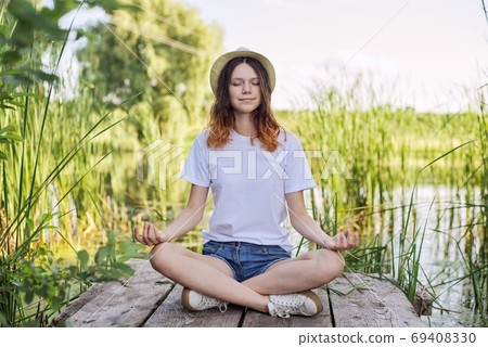 Teen girl sitting in lotus position, meditating on nature 69408330