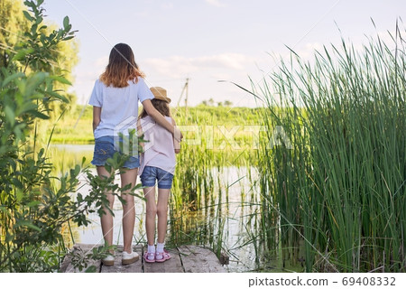 Children resting near the water on sunny summer day, back view Children resting near the water on sunny summer day, back view 69408332