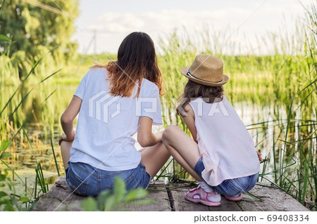 Children resting near the water on sunny summer day, back view Children resting near the water on sunny summer day, back view 69408334