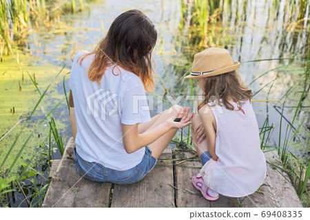 Children resting near the water on summer day, playing with water snails, back view 69408335