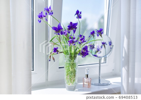 Close up of beautiful blue purple irises in a vase, perfume, make-up mirror on the window 69408513