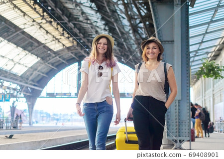 Two women mother and teenage daughter walking with luggage at railway station Two women mother and teenage daughter walking with luggage at railway station 69408901