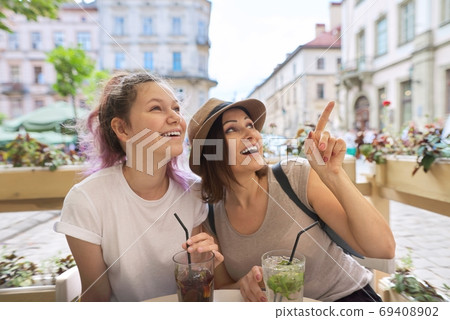 Two women in outdoor cafe talking, drinking summer ice cold drinks Two women in outdoor cafe talking, drinking summer ice cold drinks 69408902