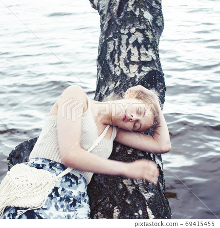 young blond woman hanging on birch tree at lake shore, summer vacations outdoor lifestyle 69415455
