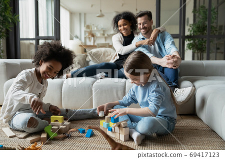 Happy mixed race parents watching children playing toys. Happy mixed race parents watching children playing toys. 69417123