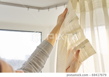 Close up of woman hands hanging curtain with metal hooks on ceiling ledge 69417679