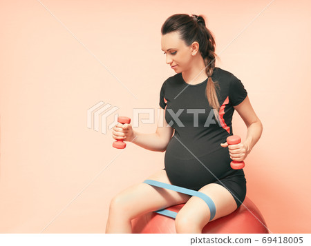 Young pregnant woman exercises with red fitball and dumbell. Working out and fitness on last months 69418005