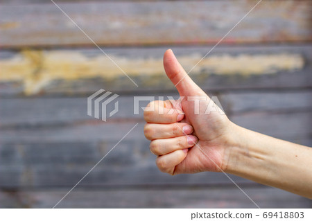 A girl or woman shows a thumbs up, class, on a wooden background. A girl or woman shows a thumbs up, class, on a wooden background. 69418803