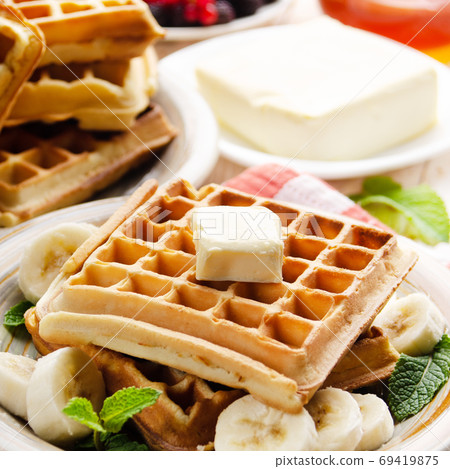 Belgian waffles served with butter banana mint leaf and syrup Belgian waffles served with butter banana mint leaf and syrup 69419875