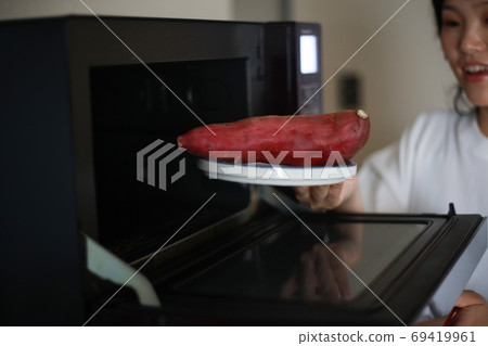 A woman trying to heat sweet potatoes in the microwave 69419961