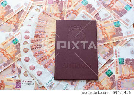 Against the background of five-thousandth bills is a red diploma with honors Against the background of five-thousandth bills is a red diploma with honors 69421496