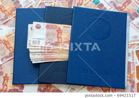 Three blue higher education diplomas lie in the background from the money, a bundle of money sticks out between the diplomas Three blue higher education diplomas lie in the background from the money, a bundle of money sticks out between the diplomas 69421517