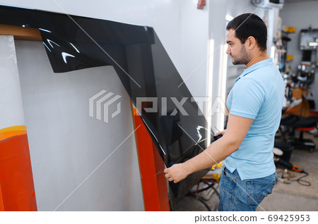 Male worker holds roll of car tinting, tuning 69425953