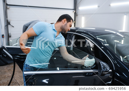 Male worker cleans car for tinting, tuning service 69425956