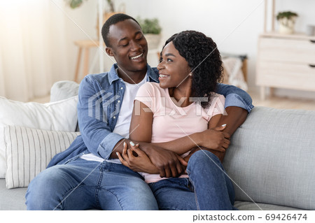 Happy african couple cuddling on sofa at home Happy african couple cuddling on sofa at home 69426474
